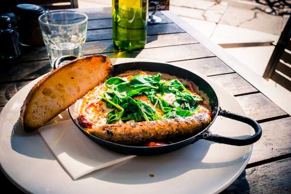 Fitzrovia Persian Baked eggs: green harissa, Persian fetta, and dukkah. Side of spiced Merguez sausage. Solo-dining accompanied by Tame Impala in the background.